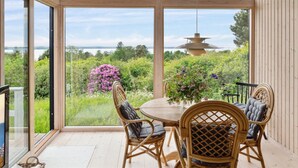 A conservatory with a wooden ceiling, large glass doors, a round table, wicker chairs, and a hanging light fixture. - "Skamhals" - 440m to the fjord by Interhome (Frederiksværk)