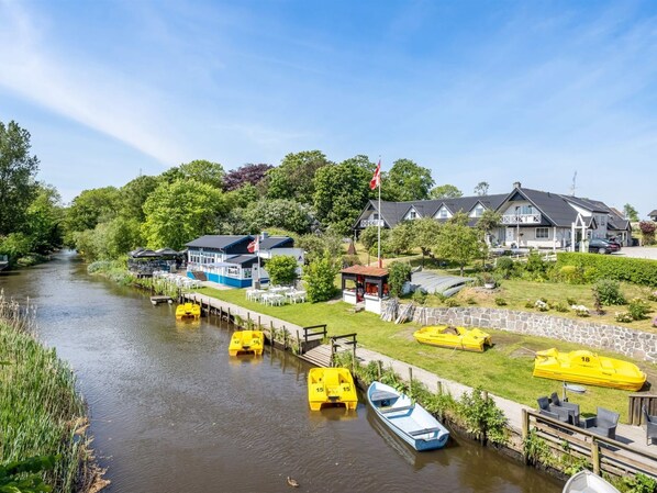 A riverside hotel with a dock, boats, and a small pavilion.