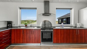 Una cocina moderna con armarios de madera, electrodomésticos de acero inoxidable y grandes ventanales con vistas al exterior.