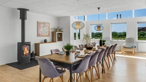 Un moderno comedor con estufa de leña, una gran mesa dispuesta para seis personas y vistas al exterior a través de amplias ventanas.