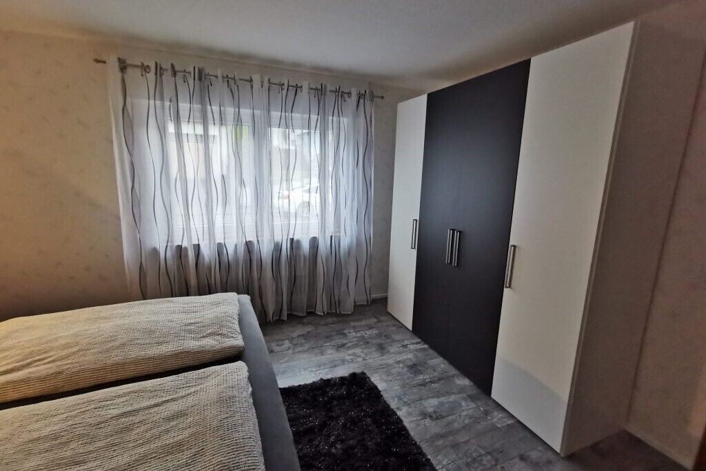 A modern bedroom with a bed, a wardrobe, and a window with sheer curtains.
