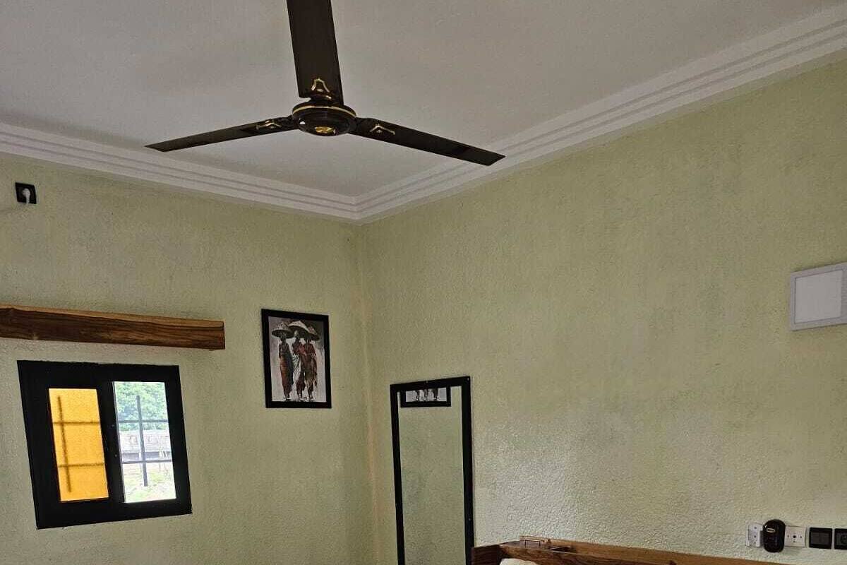 Quarto com cama, ventoinha no teto, janela e um quadro na parede.