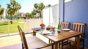 A dining area with a table set for two, a bottle of wine, and a view of palm trees and buildings. - Agua Blanca by Interhome (Dénia)