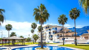 A swimming pool surrounded by palm trees and a multi-story building with balconies. - Agua Blanca by Interhome (Dénia)