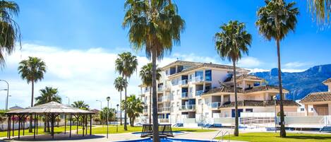 A swimming pool surrounded by palm trees and a multi-story building with balconies.