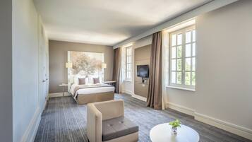 A hotel room with a bed, a sofa, a TV, a small table, and large windows.