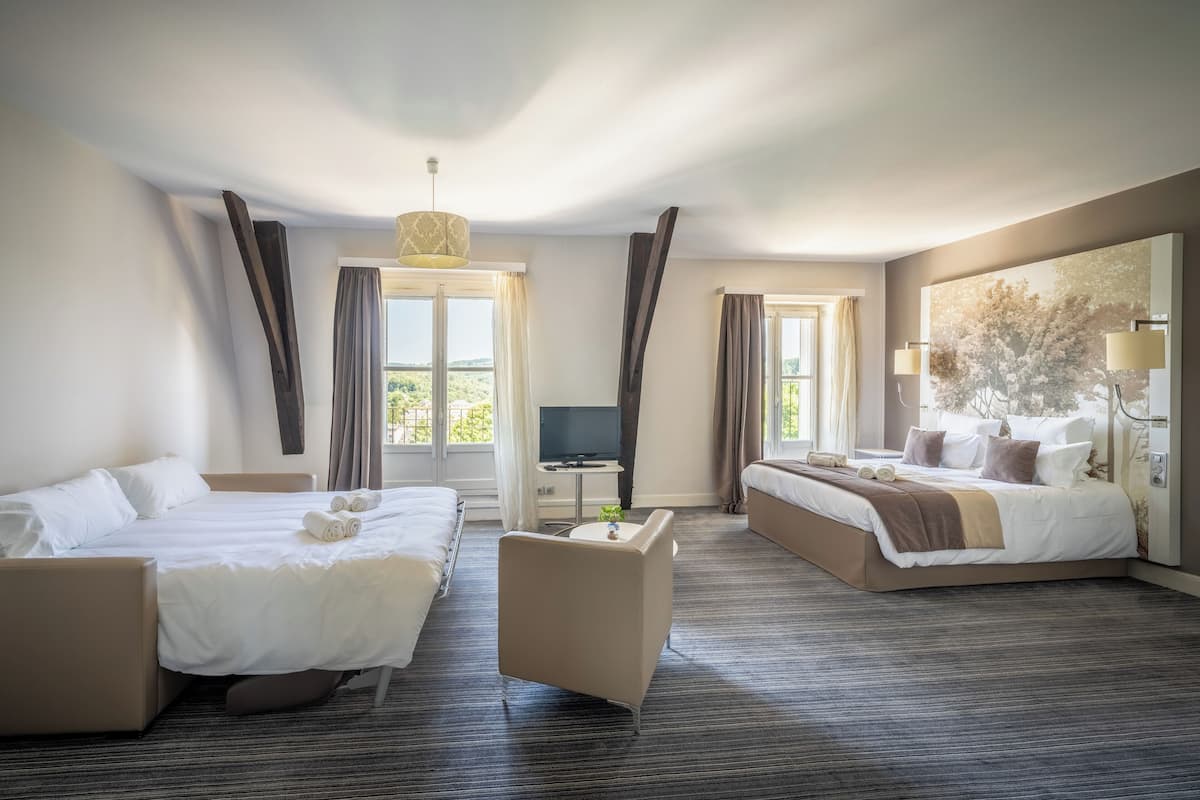 A hotel room with two beds, a sofa, a TV, and a large window with curtains.