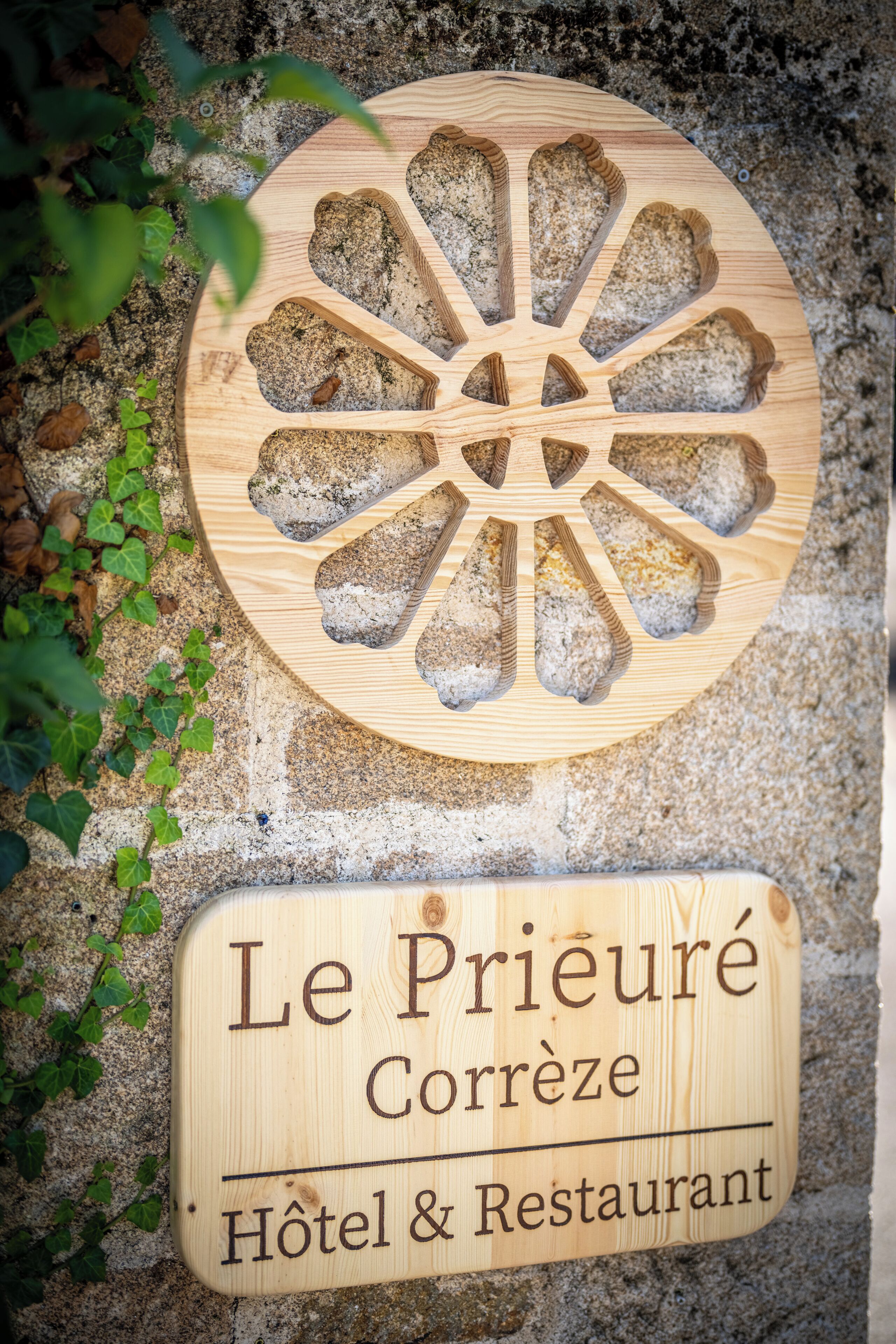 Un letrero de madera con un diseño de recorte circular y texto que indica 'Le Prieuré Corréze Hôtel & Restaurant'.