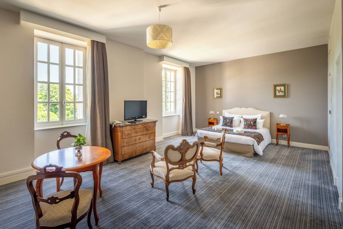A hotel room with a large bed, a television, a wooden dresser, and a dining table with chairs.