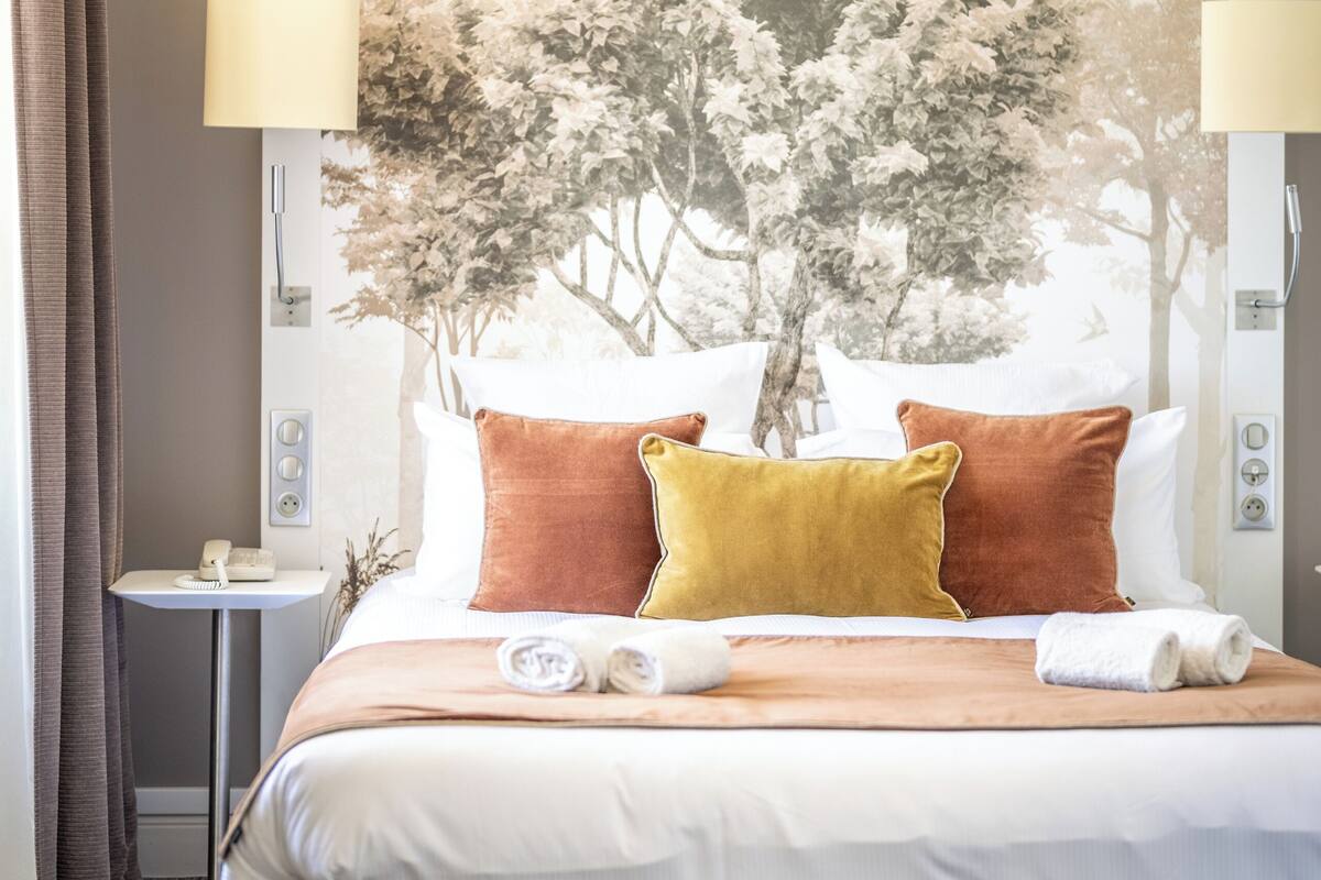 A hotel room with a large bed, two bedside lamps, a nightstand, and a wall-mounted TV.