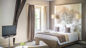 A hotel room with a bed, a TV, a small table, and a large window with curtains.
