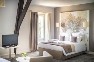 Quarto de hotel com cama, televisão, uma mesa pequena e uma janela grande com cortinas.