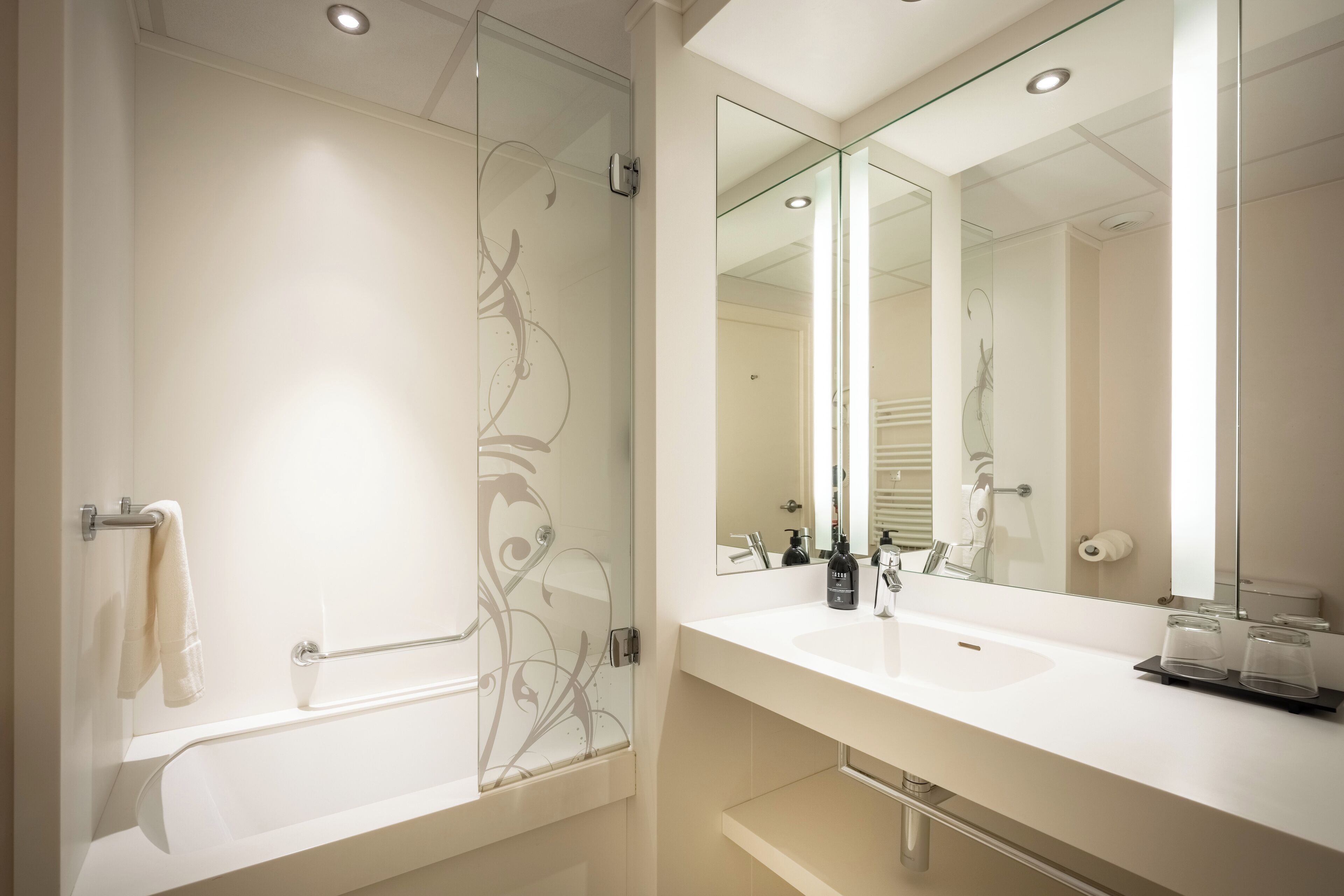 Un baño moderno con cabina de ducha de vidrio, un espejo grande y un lavabo blanco.