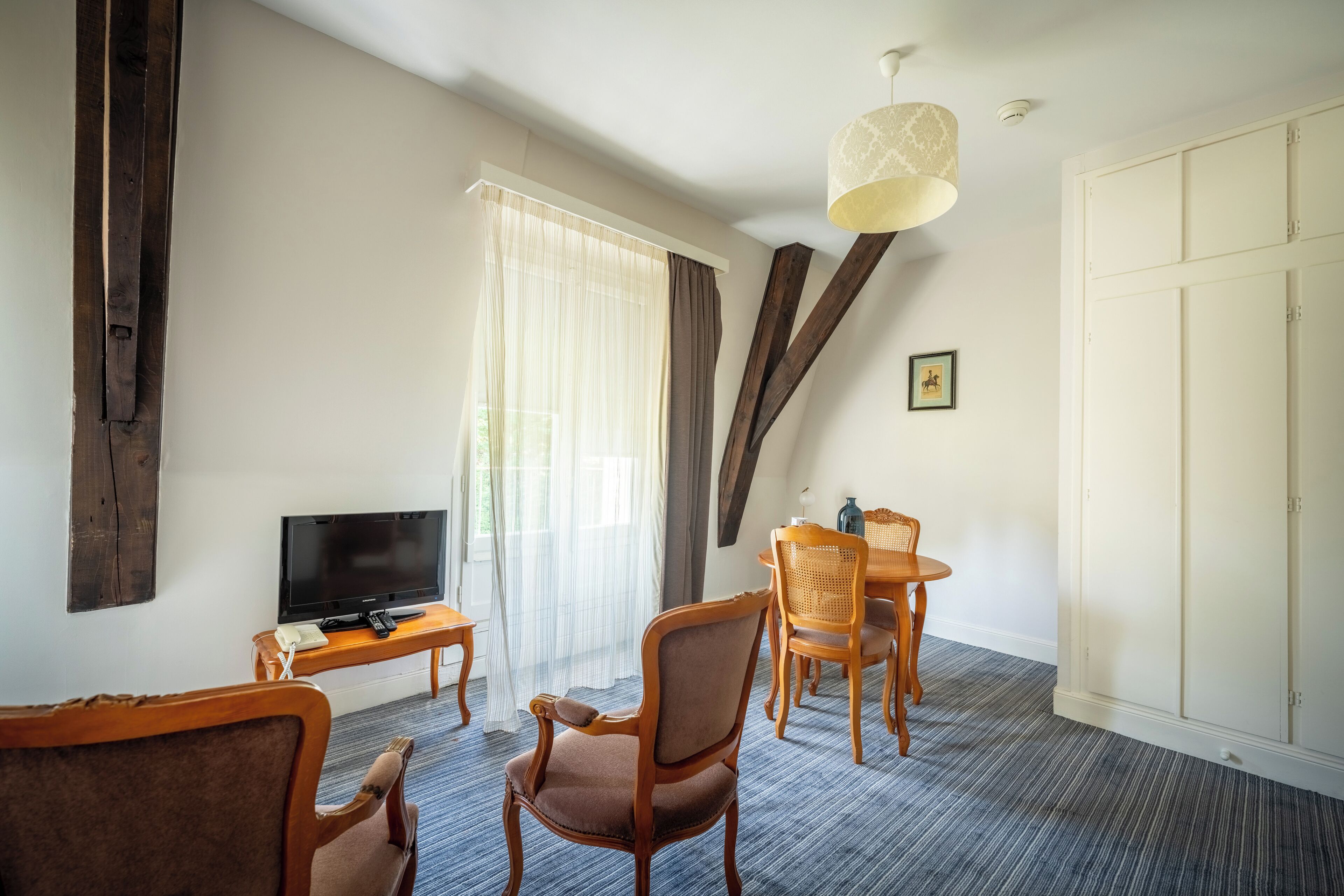 A hotel room with a TV, wooden furniture, a dining table, and a large wardrobe.