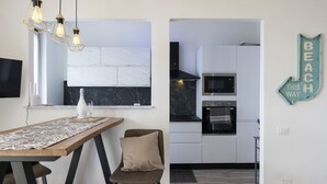 Una cocina moderna con microondas integrado, horno y salpicadero de mármol. Cuenta con una zona de comedor con mesa y sillas, y un equipo de aire acondicionado de pared.