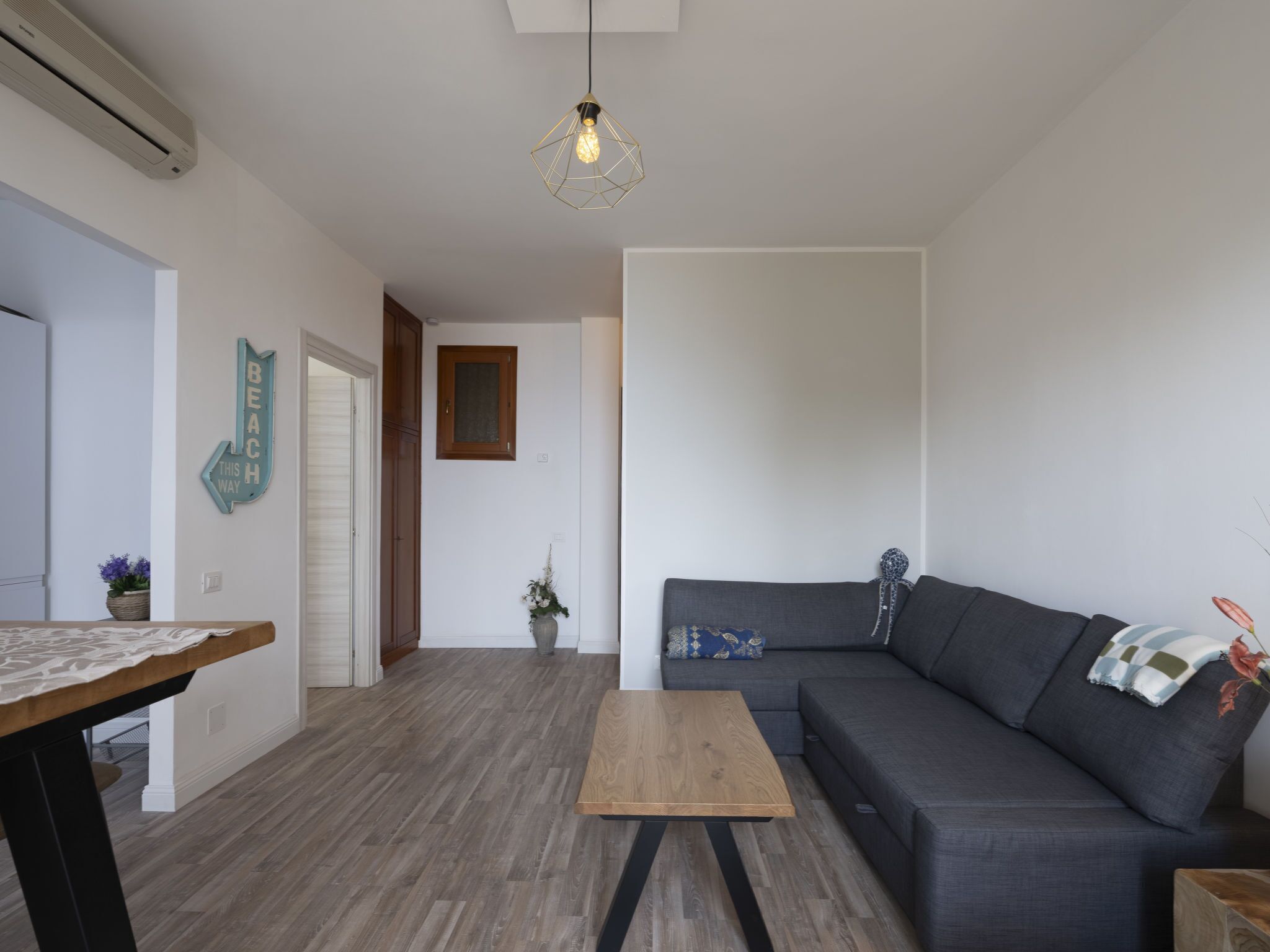 Un salón moderno con un sofá gris oscuro, una mesa de centro de madera y una lámpara colgante.