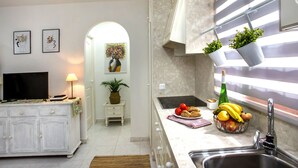 Une cuisine moderne avec des meubles blancs, un four encastré, un évier et un plan de travail agrémenté de fruits et d’une plante.