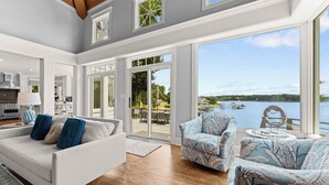 A spacious living room with a large window overlooking a lake, a dining area, and a kitchen with modern appliances. - Private Dock, Pool + HotTub, Game Room, Firepit | | Paradise Pointe by AvantStay (Sherrills Ford)