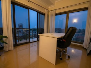 A modern office space with a large desk, black office chair, and large windows offering a city view.