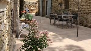 A stone building with a patio area featuring a table and chairs, a pergola, and a potted plant with flowers. - Au Cœur du Luberon, "l'atelier de La Baronnie" Charme Absolu à 4km de Gordes (Cabrières-d'Avignon)