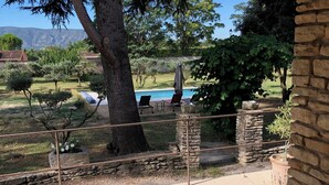 A patio with a chair, a stone wall, and a view of a swimming pool. - Au Cœur du Luberon, "l'atelier de La Baronnie" Charme Absolu à 4km de Gordes (Cabrières-d'Avignon)