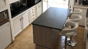 A kitchen with white cabinets, a black countertop, and a central island with bar stools. - Au Cœur du Luberon, "l'atelier de La Baronnie" Charme Absolu à 4km de Gordes (Cabrières-d'Avignon)