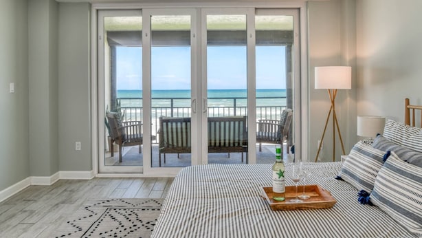Ein Hotelzimmer mit einer großen SchiebeglasTür, die auf einen Balkon mit Blick auf den Strand führt.