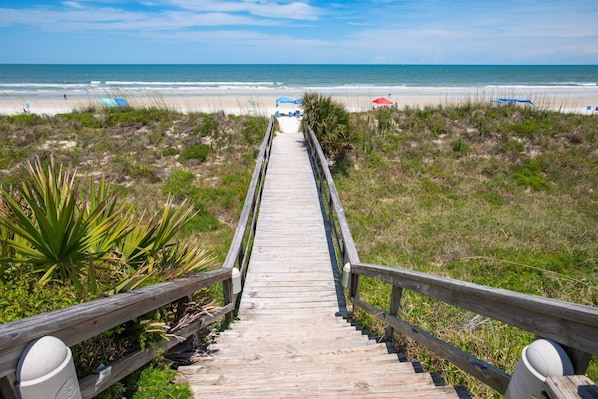 A wooden boardwalk leading to a beach with umbrellas and chairs.