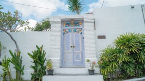 Un bâtiment blanc avec une porte bleue, des plantes en pot et un palmier.