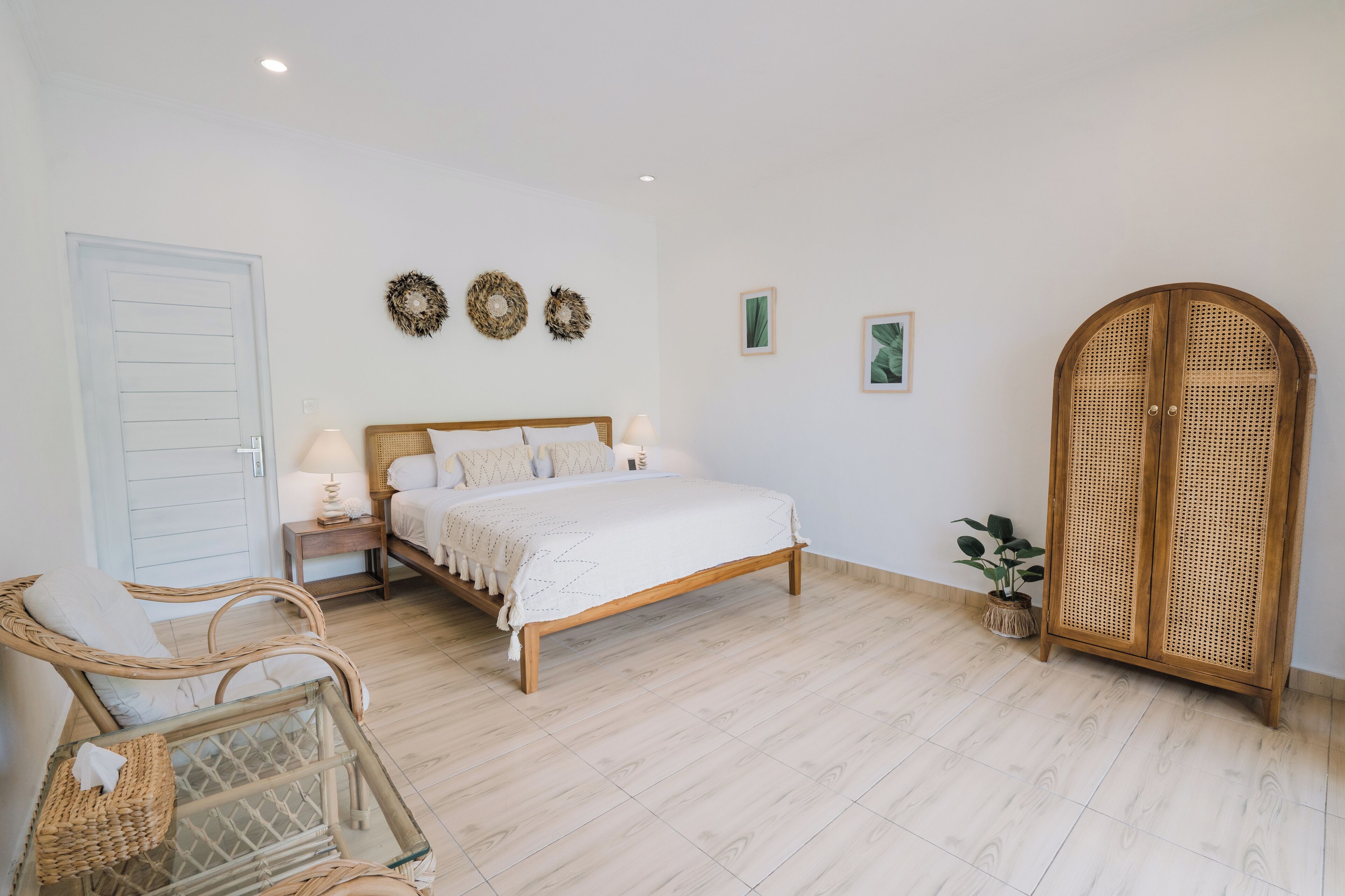 Un dormitorio con cama, mesitas de noche, una silla de mimbre, un armario y una planta en maceta.