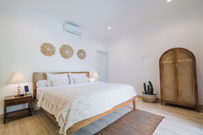 A bedroom with a bed, bedside tables, a lamp, a rattan wardrobe, and a cactus plant.