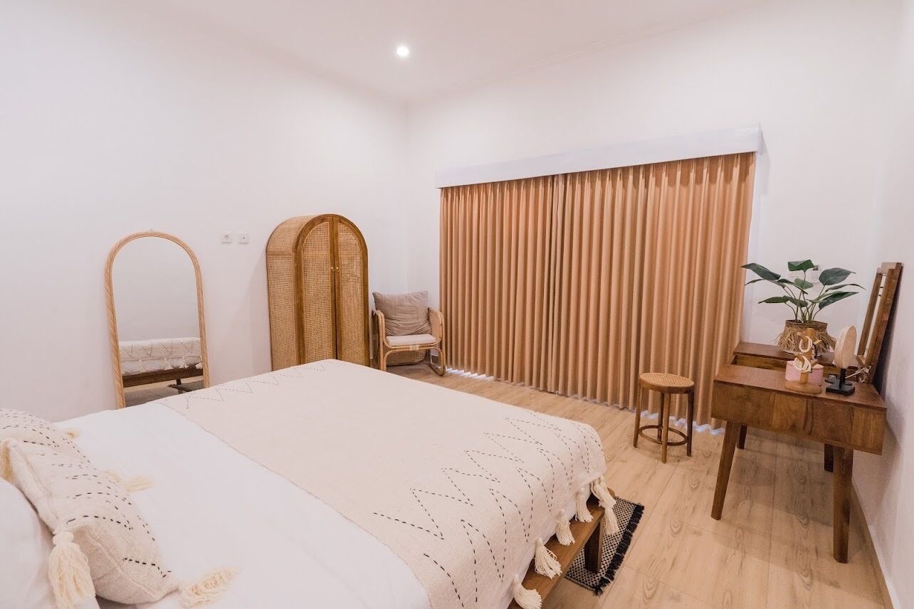 Un dormitorio con cama, un escritorio de madera, una silla, un espejo y una ventana con cortinas.