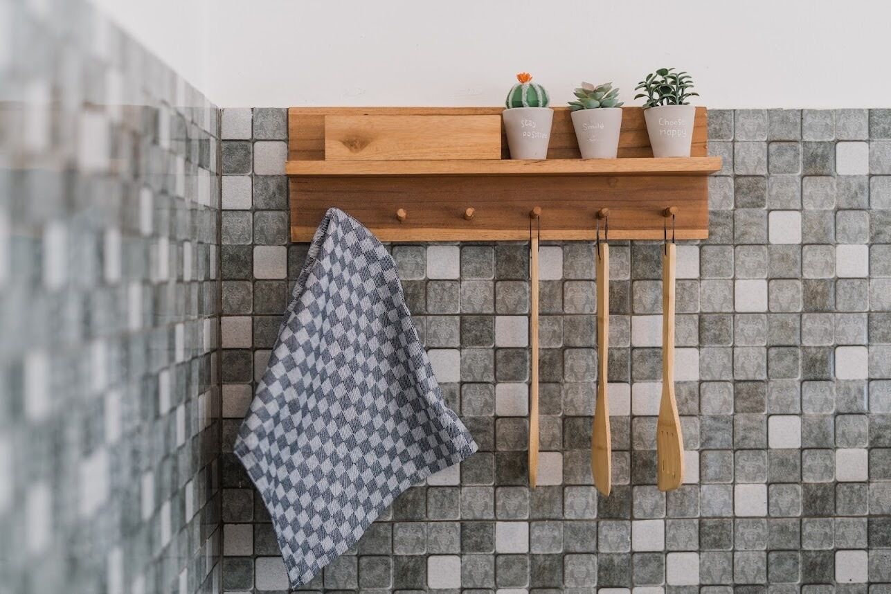 A kitchen with a wooden shelf holding three potted plants and a hanging wooden spoon rack.