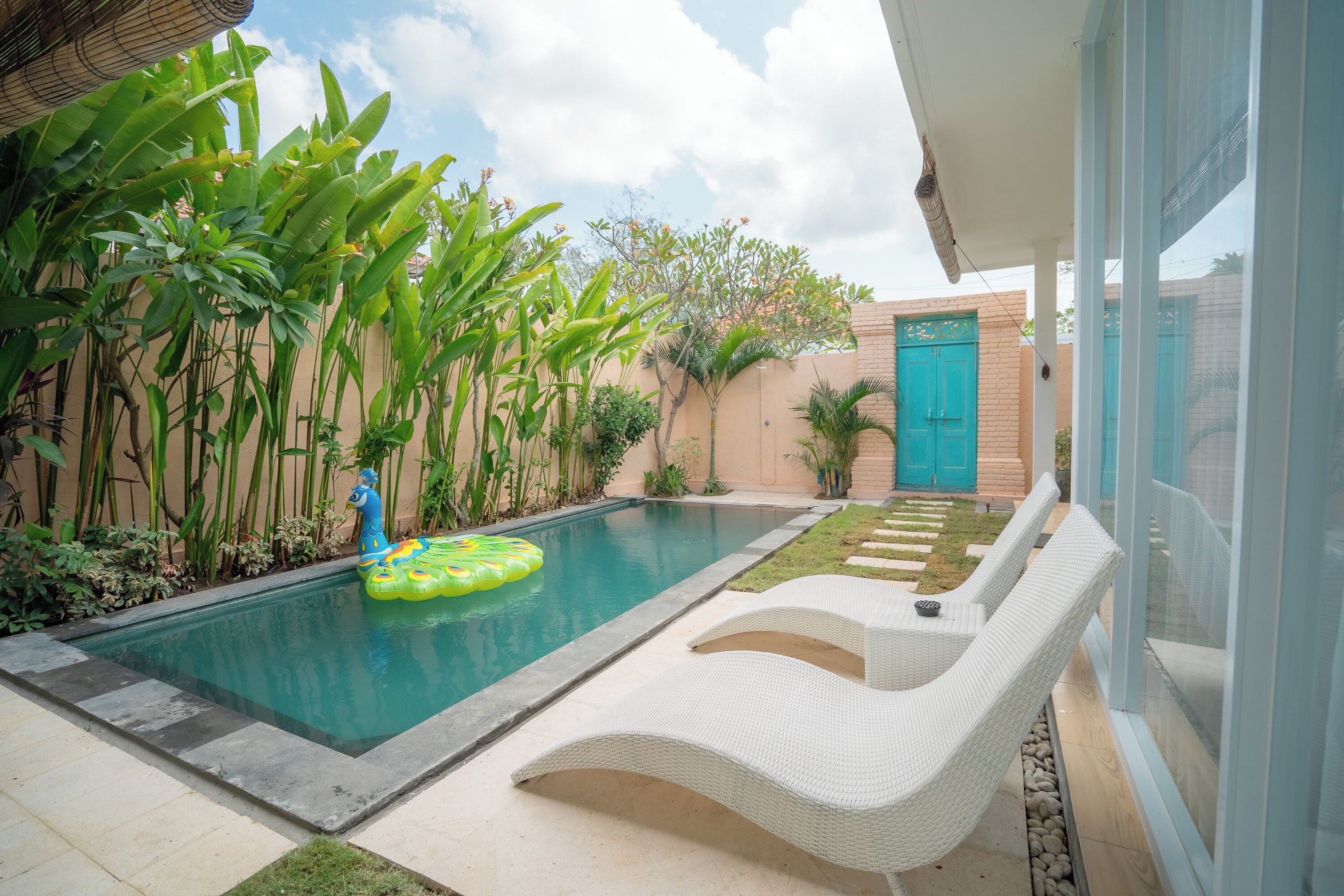 A swimming pool with a floating ring, surrounded by lush greenery and a white lounge chair.
