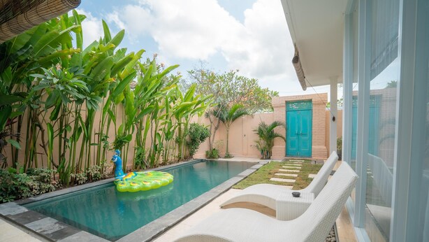 Une piscine avec un flotteur gonflable vert, entourée d’une végétation luxuriante et agrémentée d’un fauteuil de relaxation blanc.