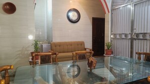 A room with a glass table, wooden chairs, a brown sofa, and a clock on the wall. - Star Residency (Varanasi)