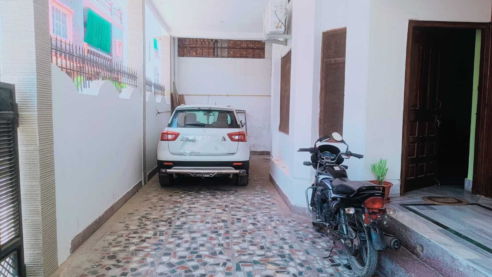 A narrow alleyway with a white car parked at the end and a motorcycle on the right.