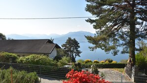 Uma casa com telhado de cerâmica, rodeada por vegetação e vista para montanhas e um lago.