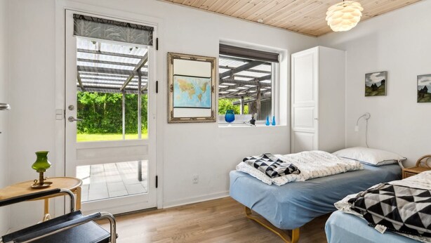 A bedroom with two beds, a wooden ceiling, a globe on the wall, and a view of greenery outside.