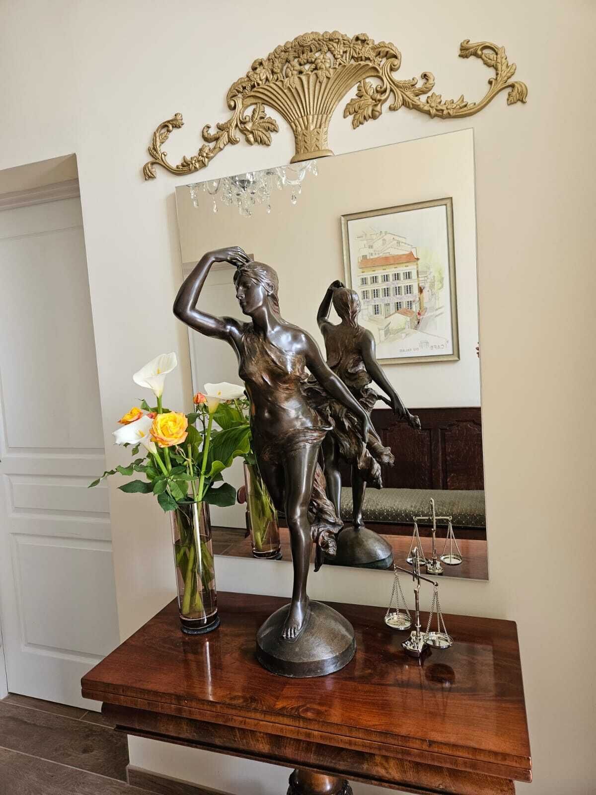 A wooden table with a bronze statue of a woman, a vase of flowers, and a framed architectural drawing.