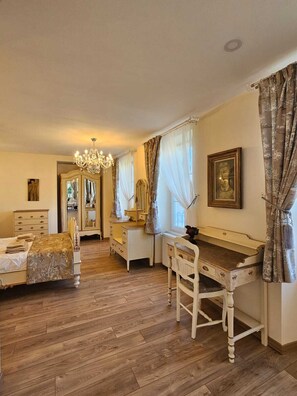 Une chambre avec un plancher en bois, un lit recouvert d’une couverture dorée, une commode, une coiffeuse avec un miroir et un bureau avec une chaise.