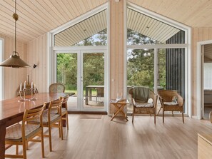 A spacious dining area with a wooden table and chairs, large windows, and a view of the outdoors.