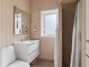 A bathroom with a wooden wall, a white sink, a mirror, and a shower curtain.