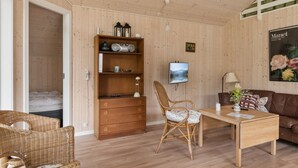 A room with a wooden floor, a bed, a wooden bookshelf, a wicker chair, a table, a brown leather sofa, and a wall-mounted TV. - "Vojdan" - 600m from the sea by Interhome (Fårevejle)