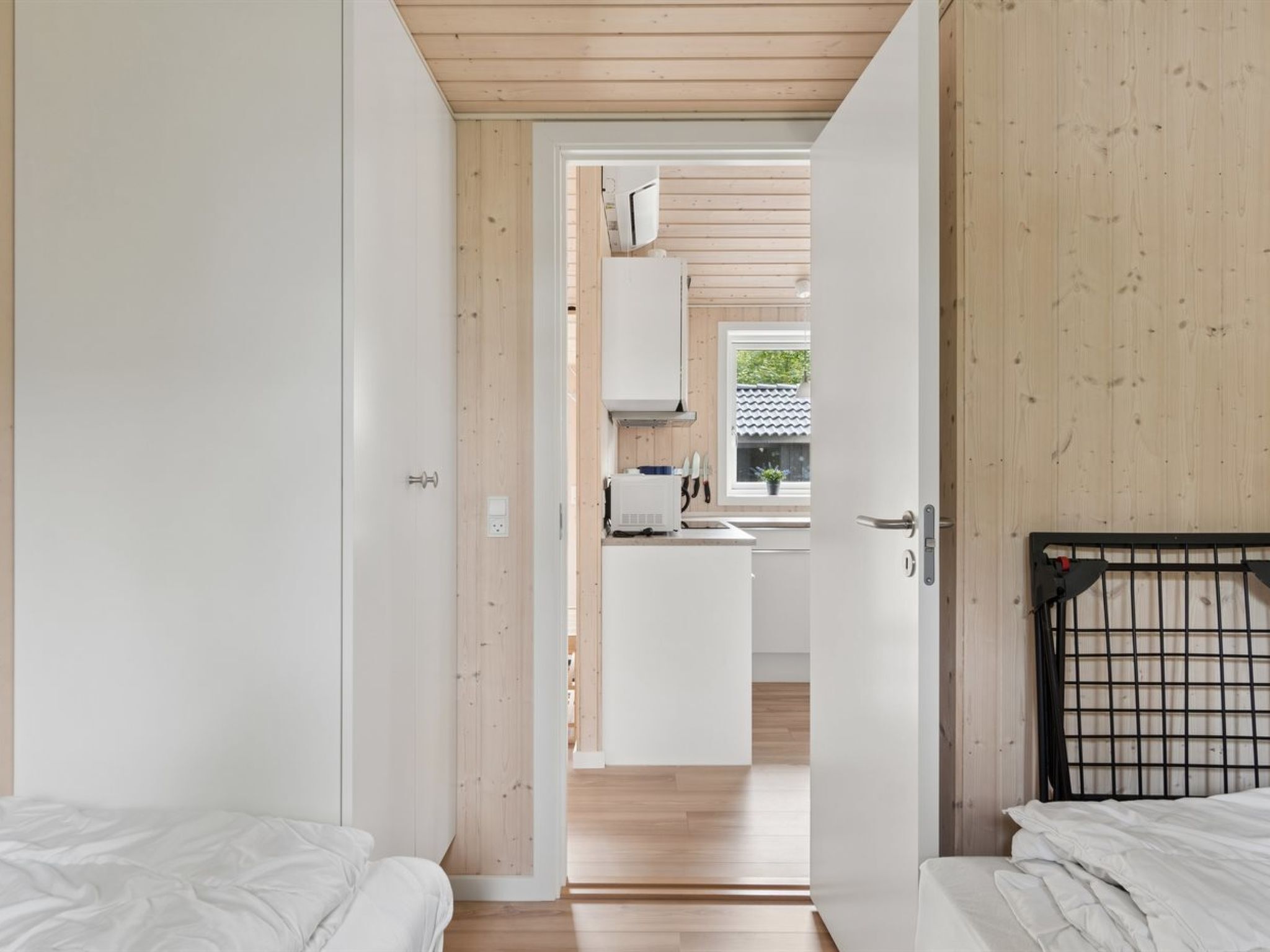 Quarto com duas camas, teto de madeira e vista para uma cozinha.
