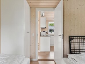 A room with two beds, a wooden ceiling, and a view into a kitchen area.
