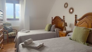 A bedroom with two beds, a chair, a dresser, and a nightstand with a lamp.