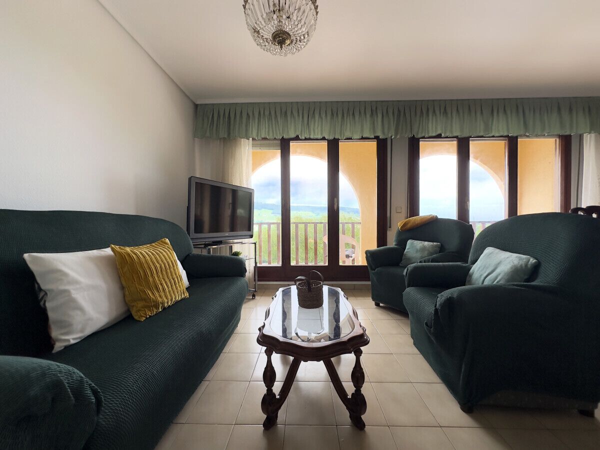 A living room with a green sofa, a glass coffee table, and a television on a stand.