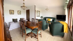 A dining area with a wooden table and chairs, a sofa, a television, and framed pictures on the wall.