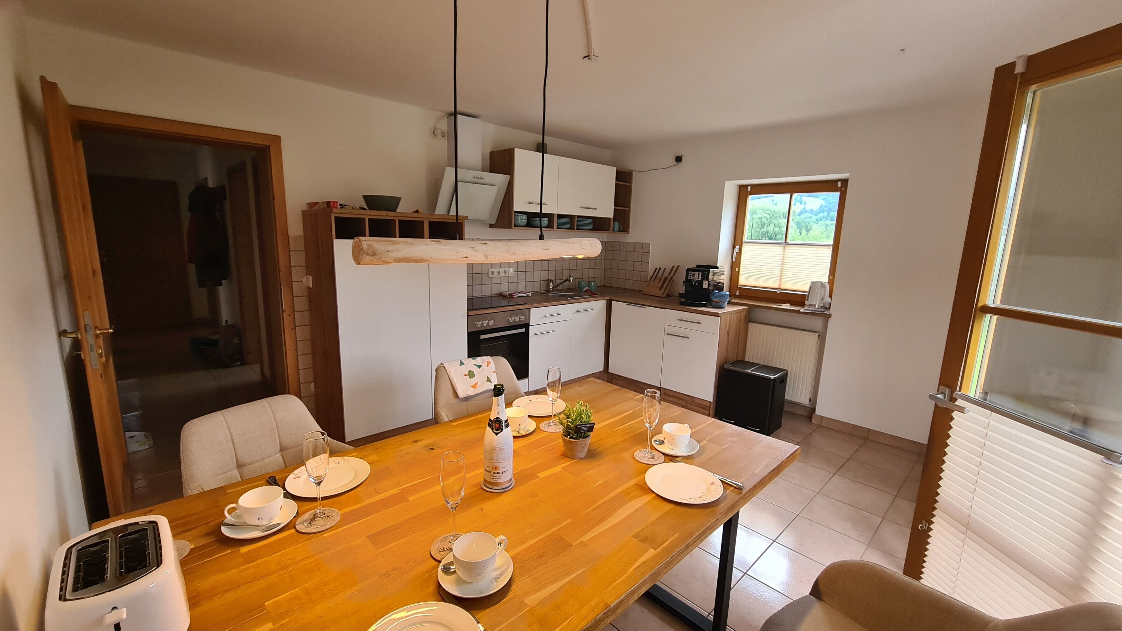 A modern kitchen with wooden cabinets, a dining table set for four, and a view of the outdoors through a window.